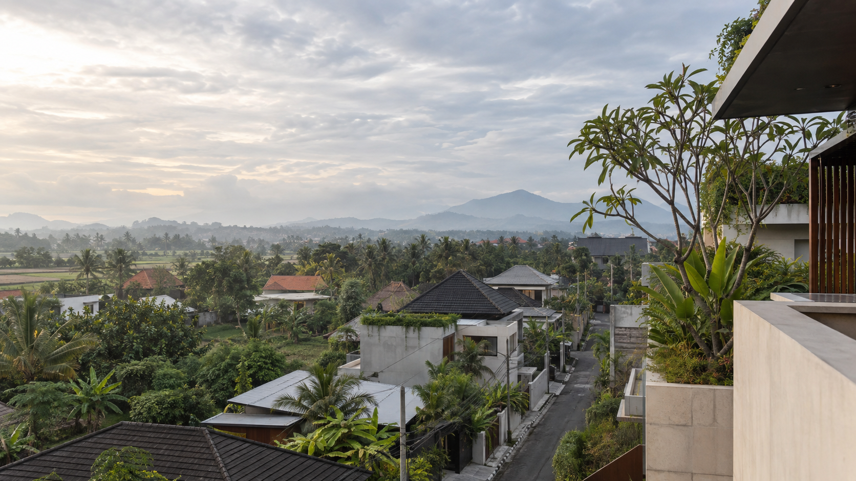 View over villa rooftops, palms and rice fields towards the mountains in Bali